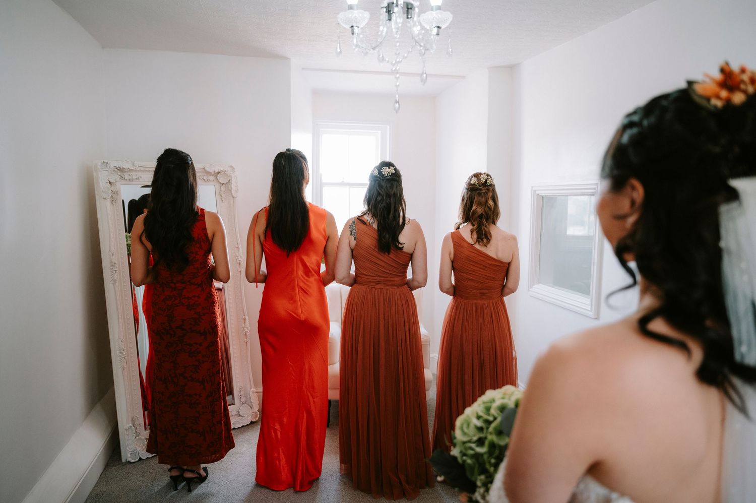 Bridesmaids in matching red dresses stand together in bright white room.