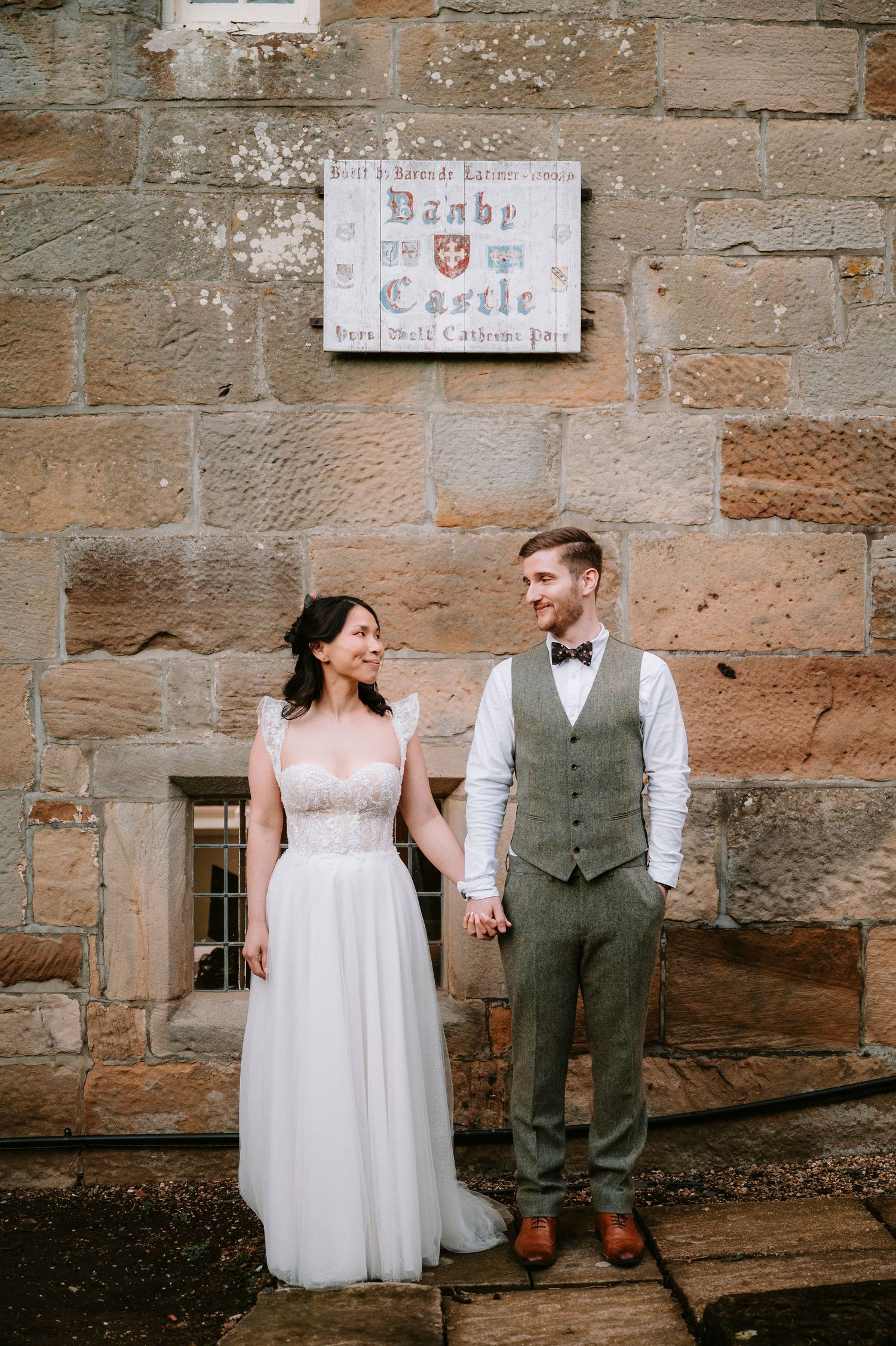 Couple poses against rustic stone wall during wedding photoshoot.