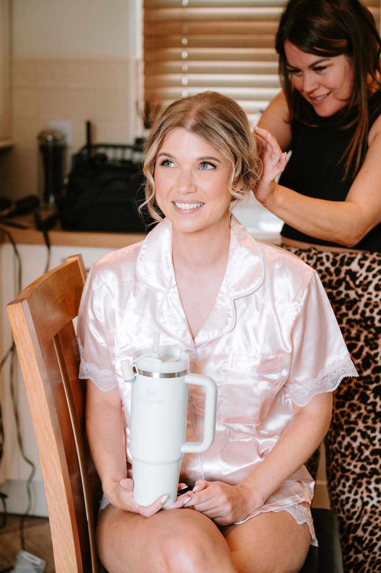 Bridal party in satin robes enjoying drinks during wedding morning preparations.