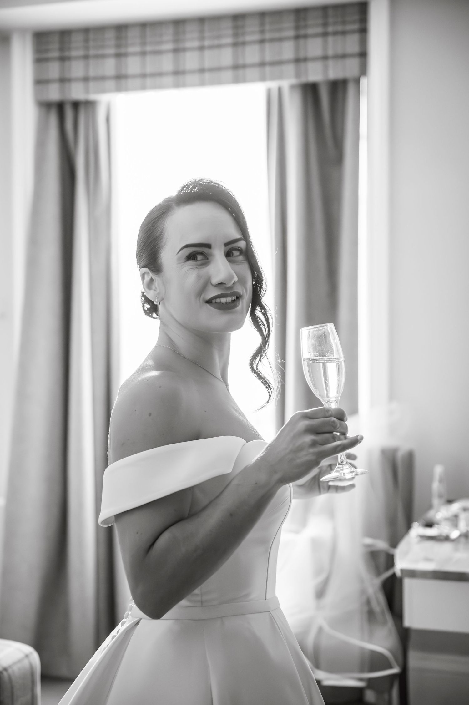 Getting ready sequence showing final adjustments to a white wedding dress in a sunlit room.