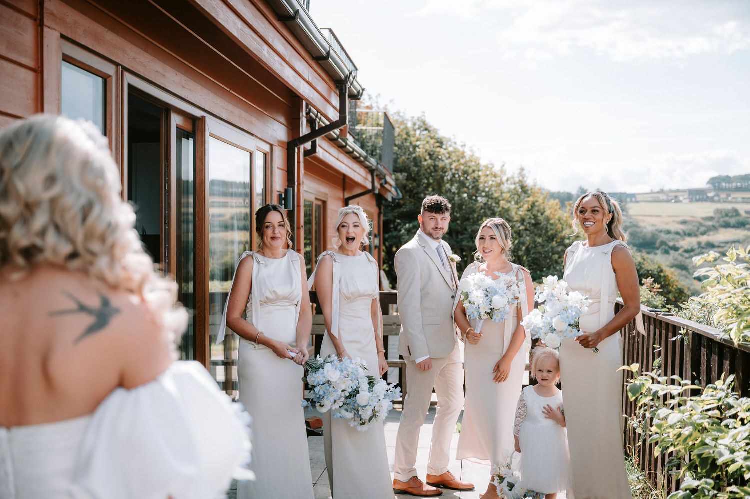 Wedding party poses on wooden deck with scenic mountain views in background.