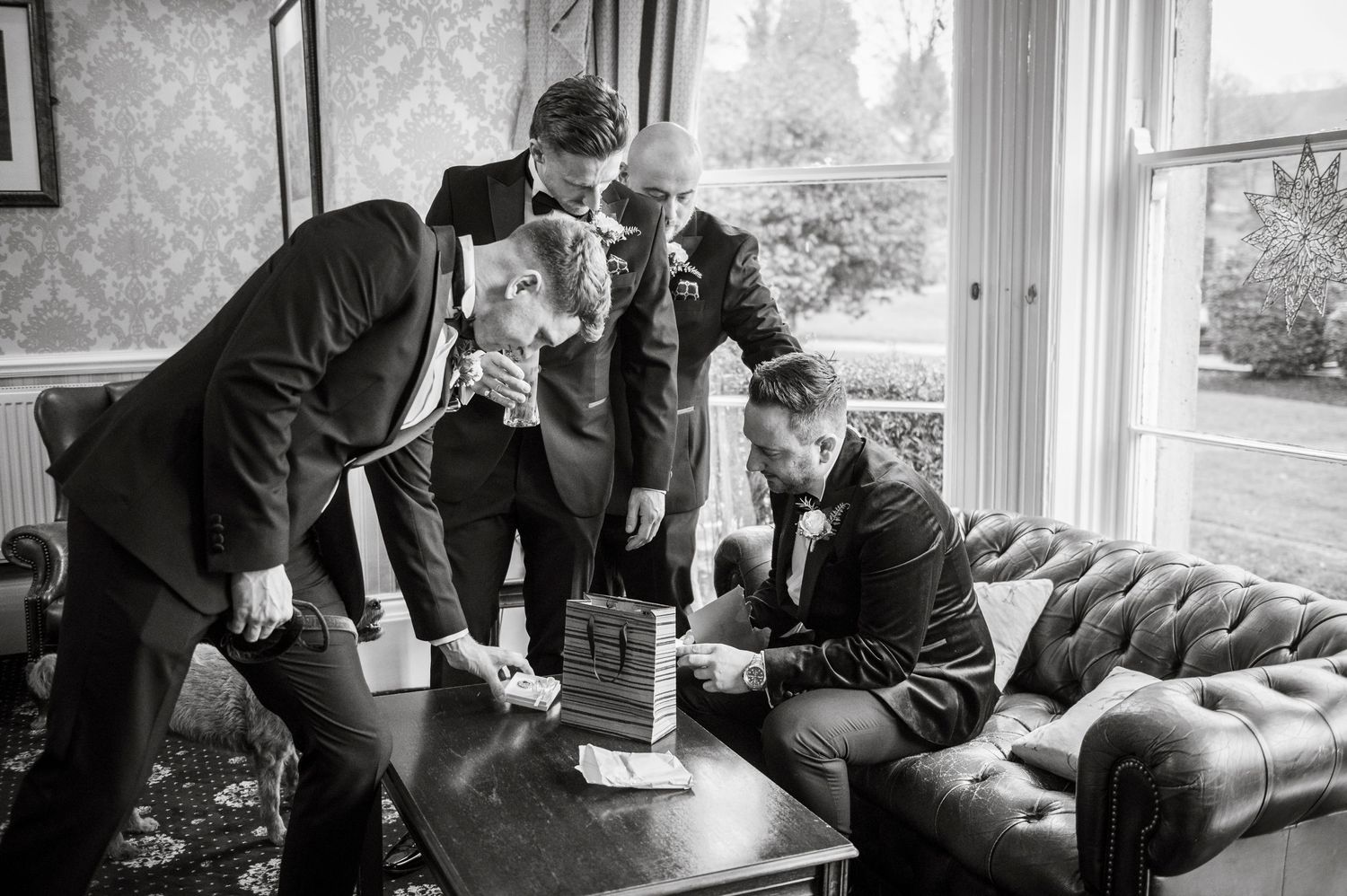 Groomsmen lounge and socialize in an elegant room with ornate wallpaper.