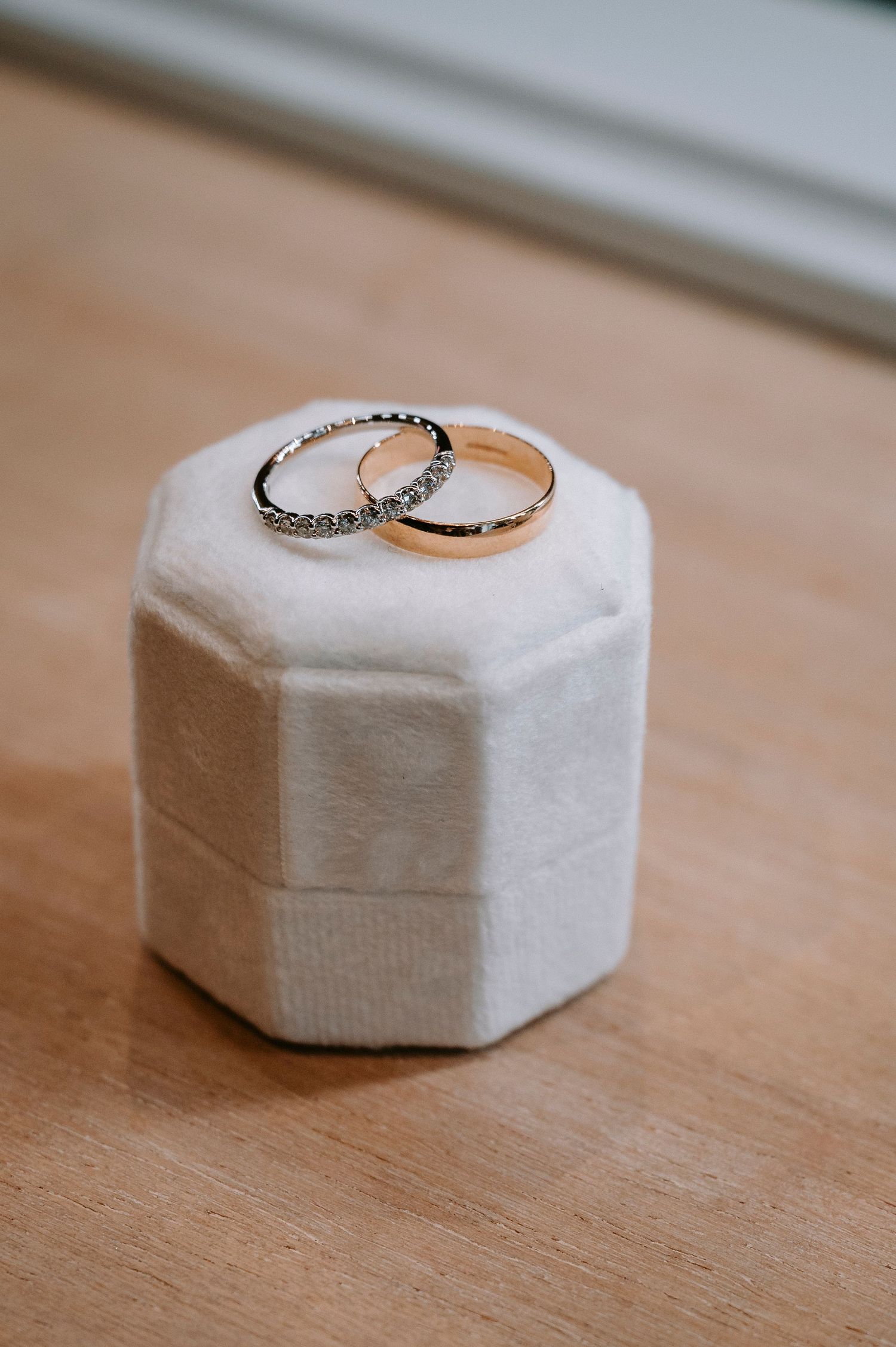 Wedding rings displayed on white hexagonal ring boxes on wooden surface.