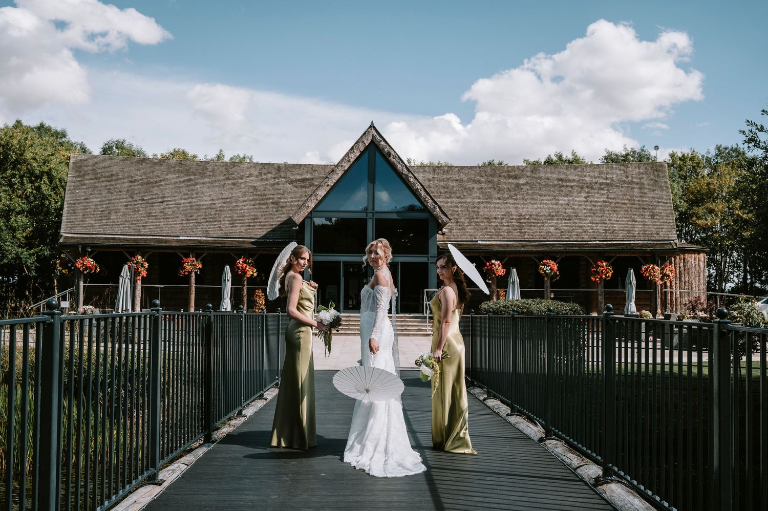 Wedding party members walk through a garden pathway surrounded by black metal fencing on a sunny afternoon.
