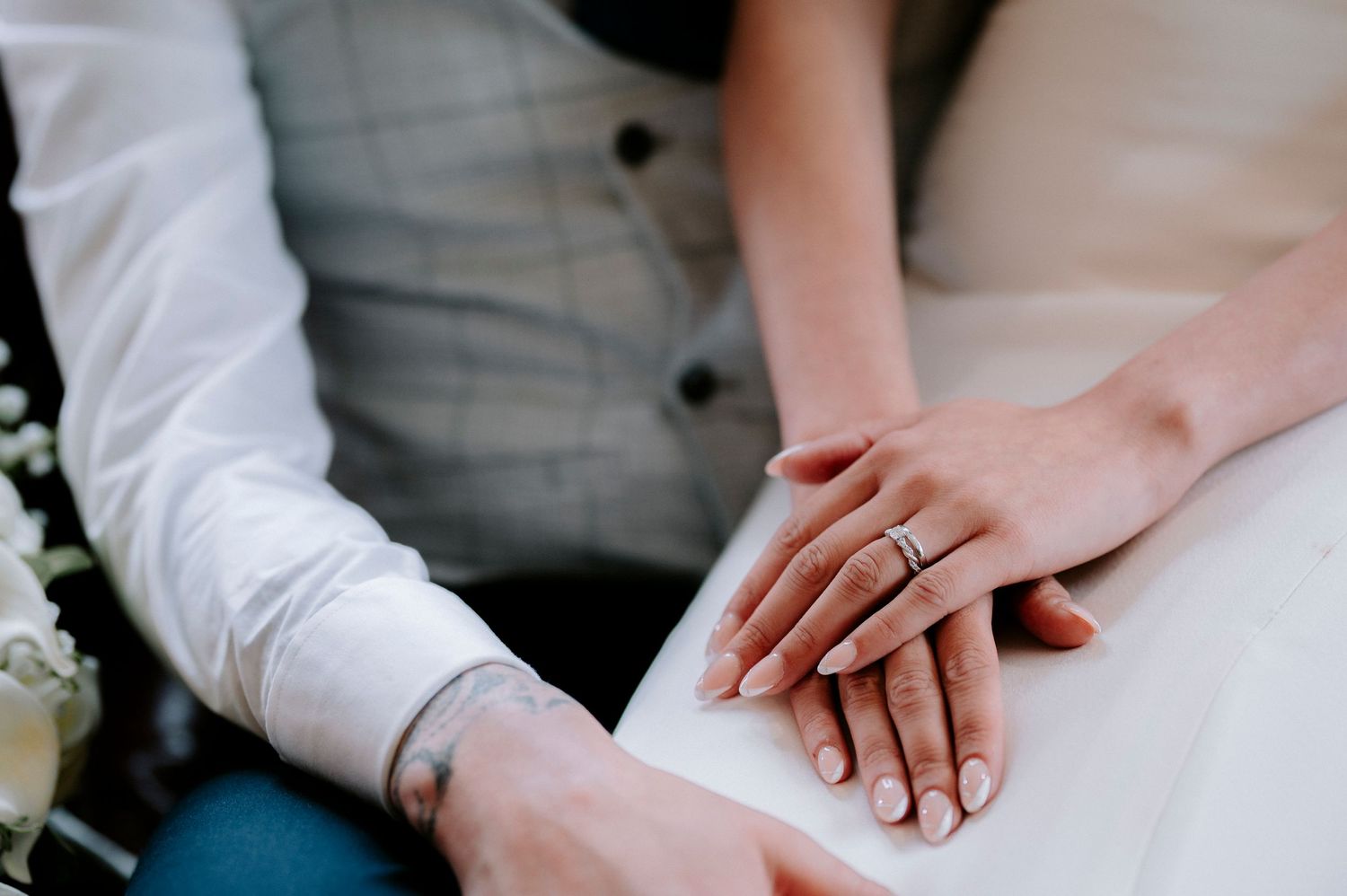 Close-up of wedding rings and hands resting on white fabric.
