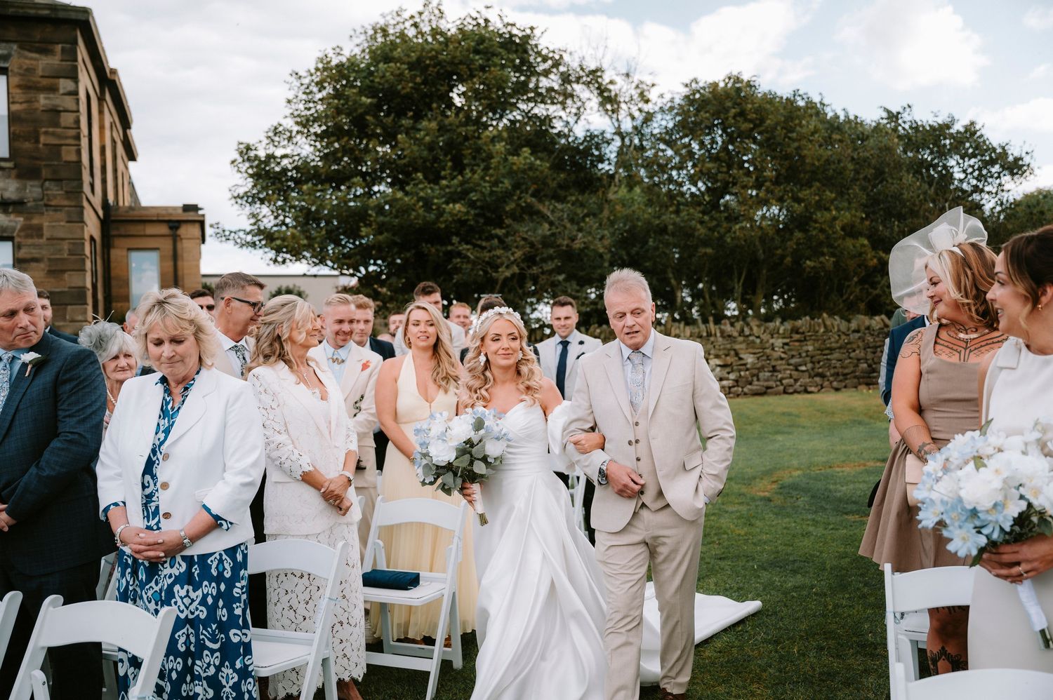 A wedding party celebrates outdoors with joyful expressions and light blue accents in their attire.