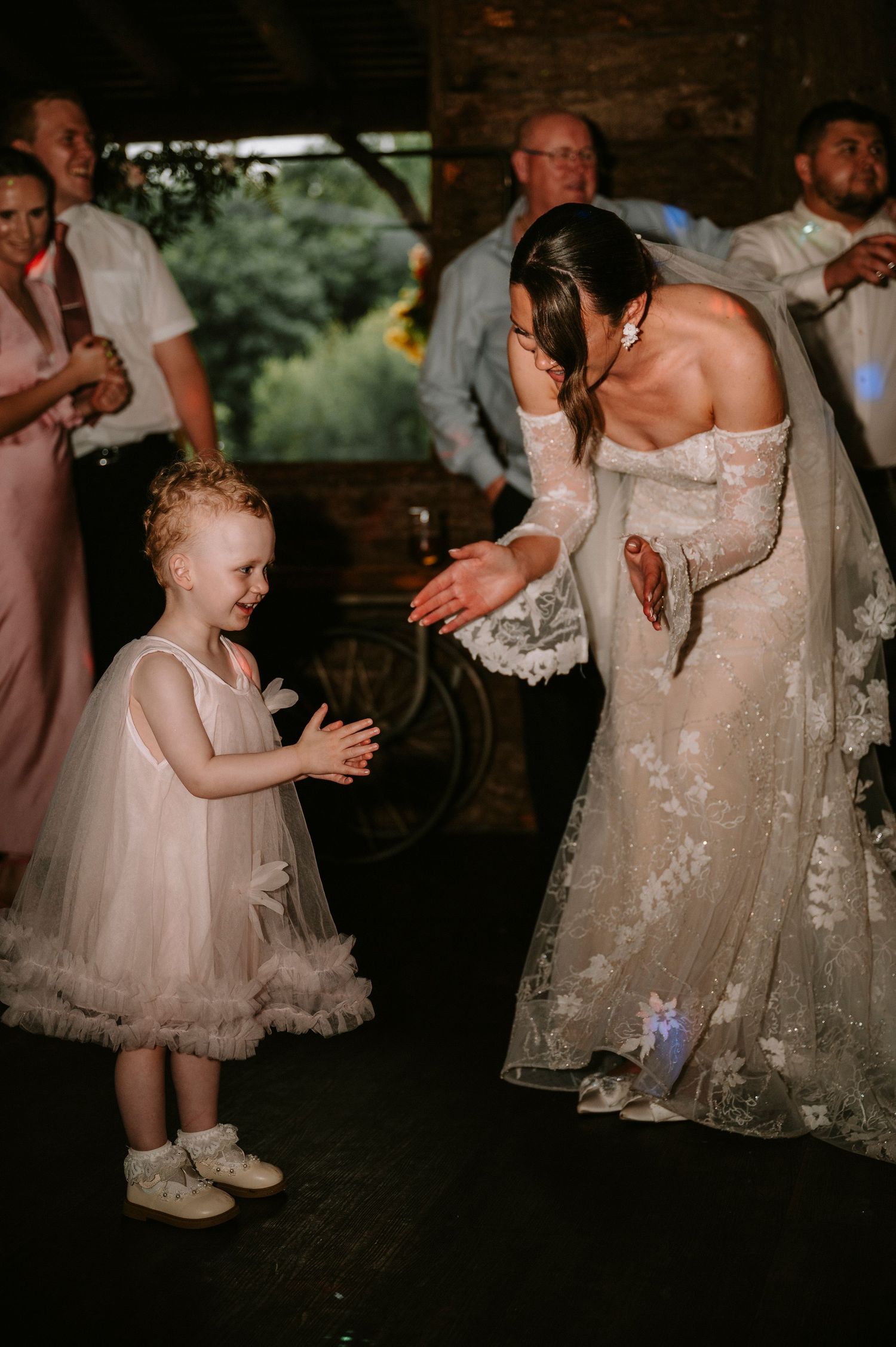 Young flower girl in tulle dress dances with bride in lace gown.