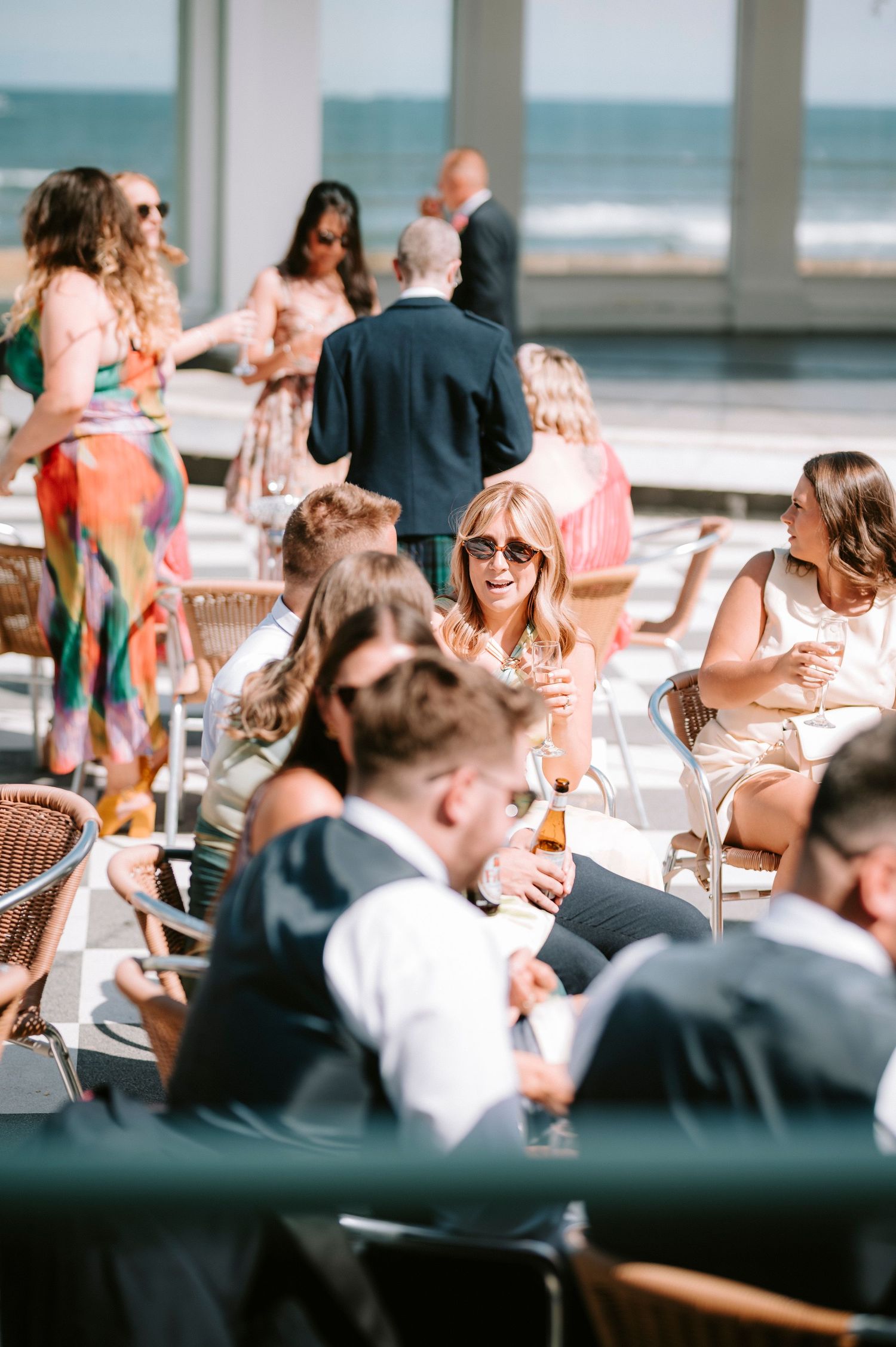 Wedding guests enjoying a casual outdoor reception by the beach on a sunny afternoon.