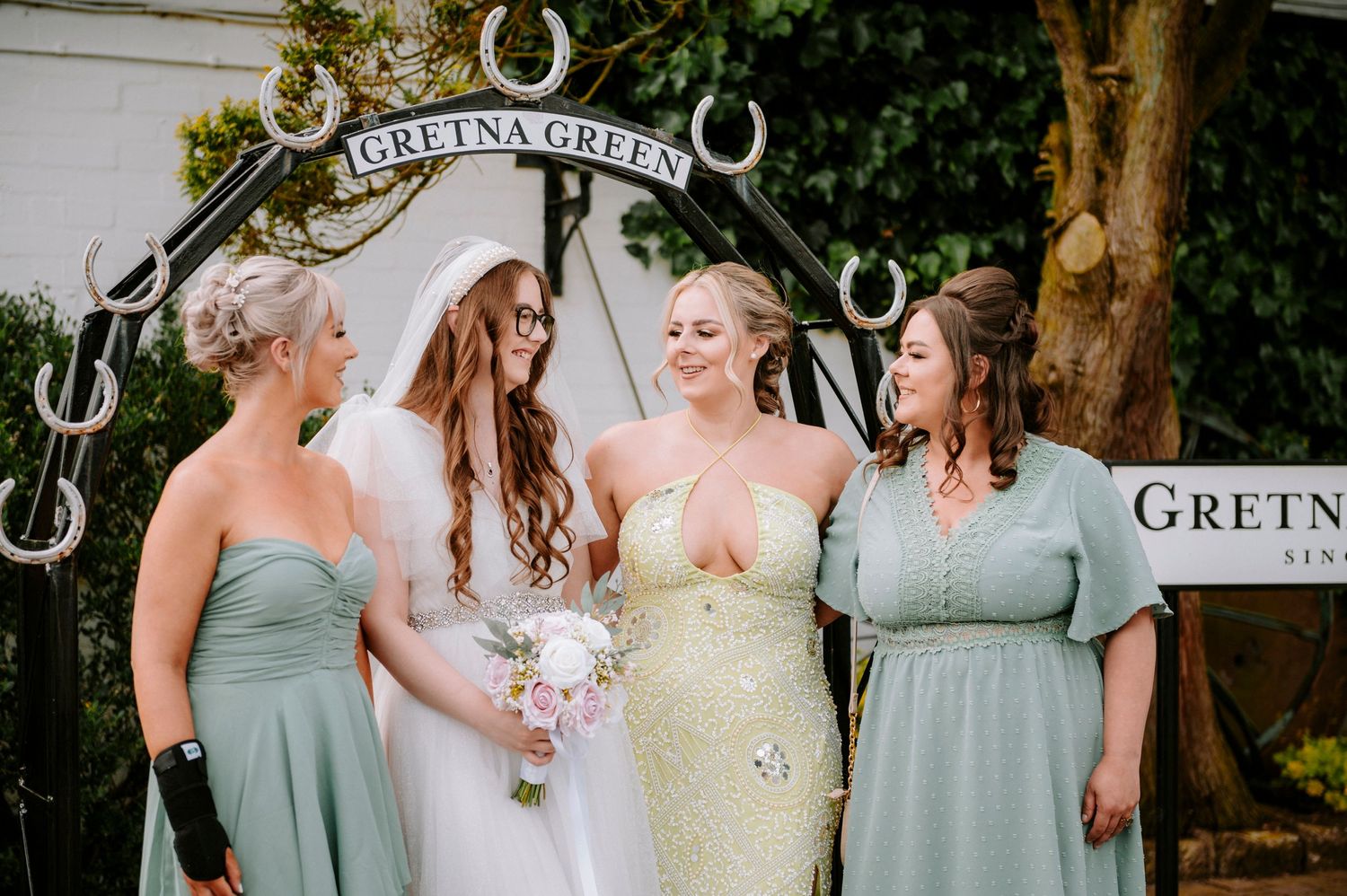 Wedding party in sage green dresses posing under the Gretna Green archway.