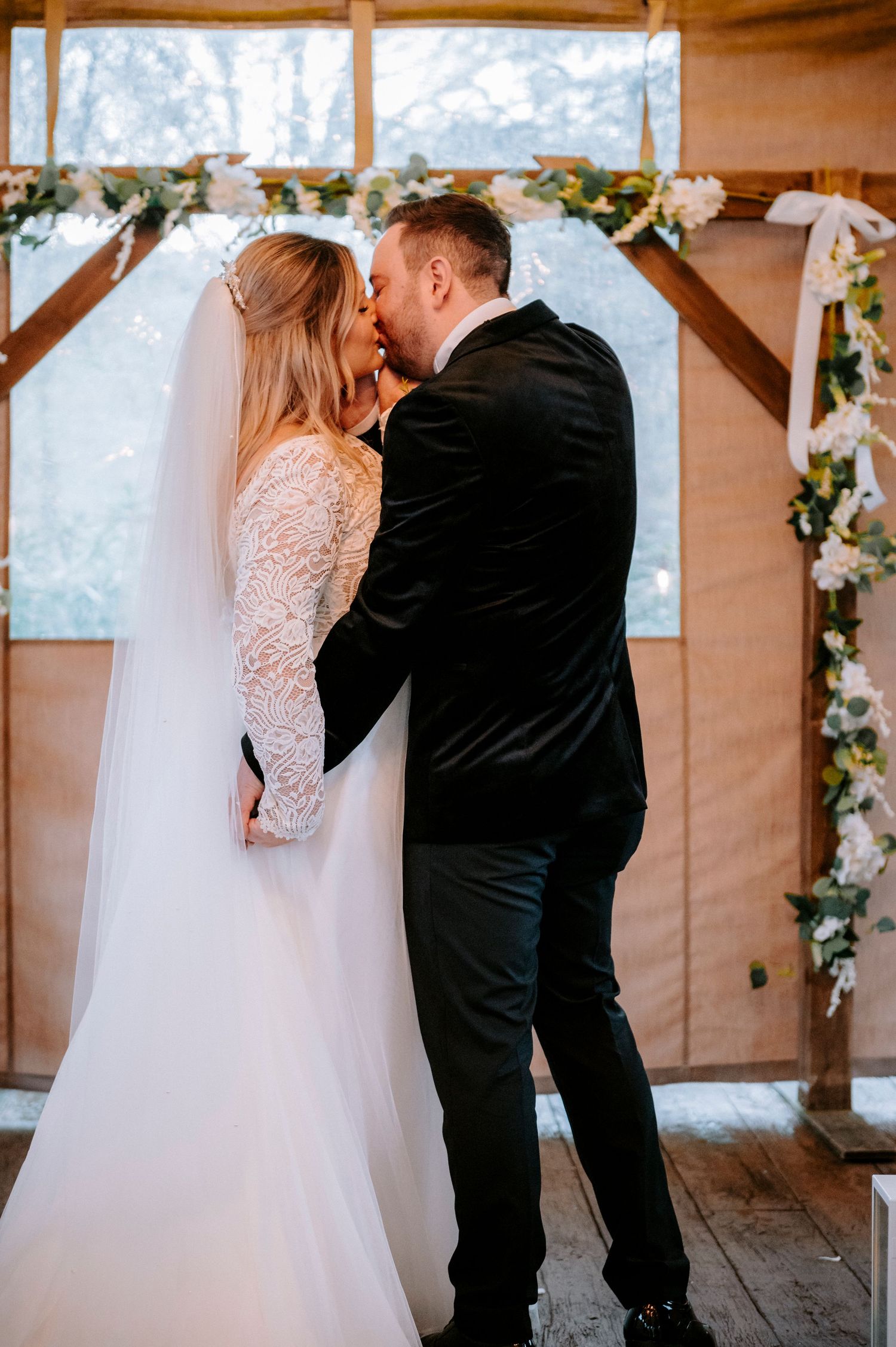 Wedding couple sharing a romantic moment in a rustic wooden venue decorated with floral garlands.