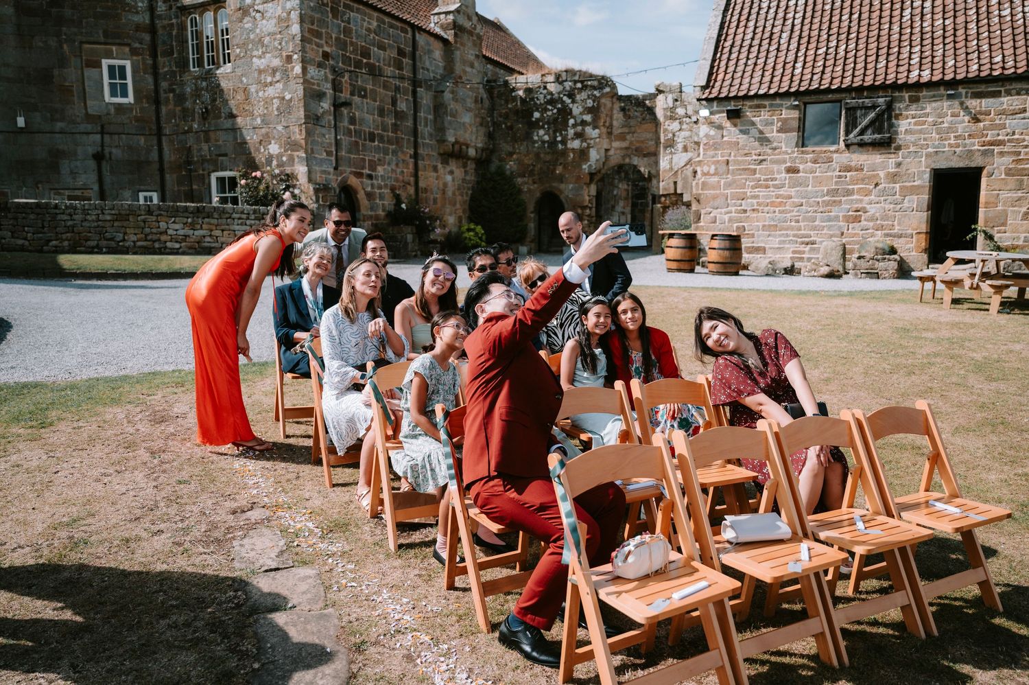 Wedding guests seated on wooden chairs at an outdoor rustic stone venue.