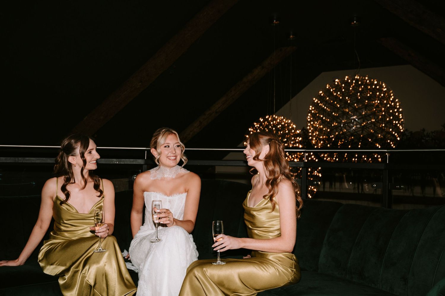 Bridesmaids in gold dresses and bride in white gown laugh together during wedding reception celebration.