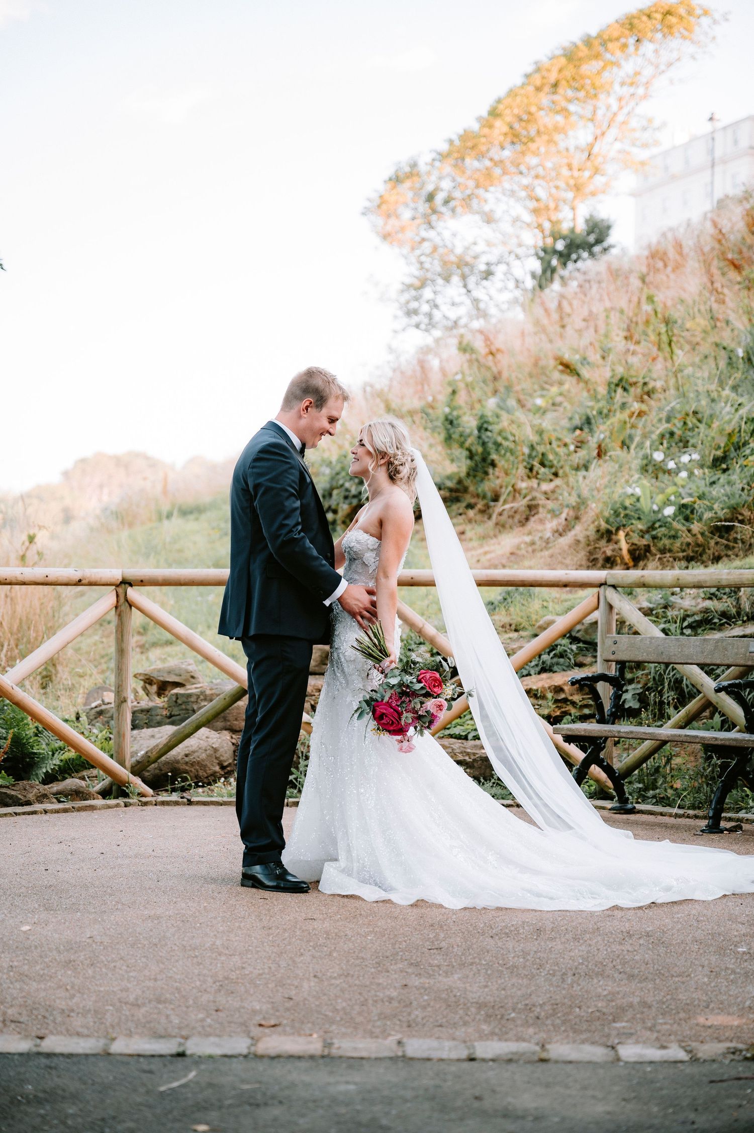 Wedding couple shares intimate moments on rustic wooden bridge during autumn.