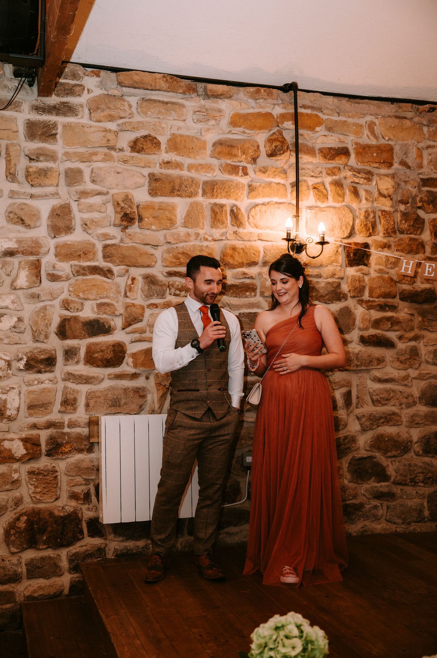 A couple shares an intimate moment against a rustic stone wall backdrop with warm lighting.