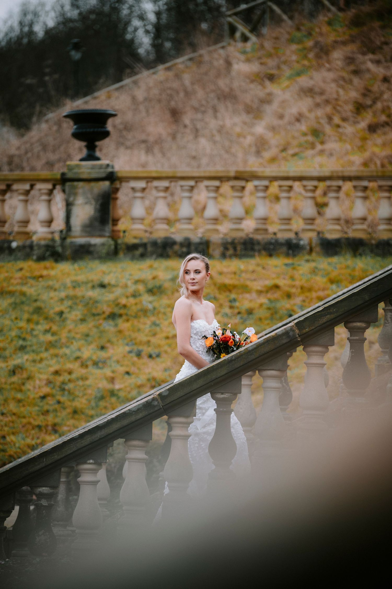 A dramatic wedding photo featuring a stone balustrade and autumn landscape backdrop.