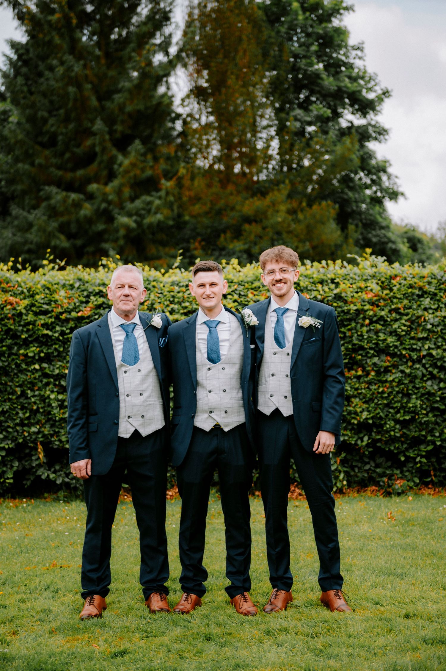 Groomsmen in matching navy suits and grey vests pose together outdoors.