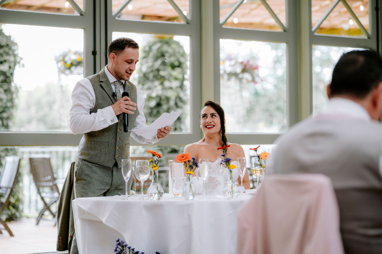 Wedding reception venue with elegant table settings and natural light streaming through large windows.