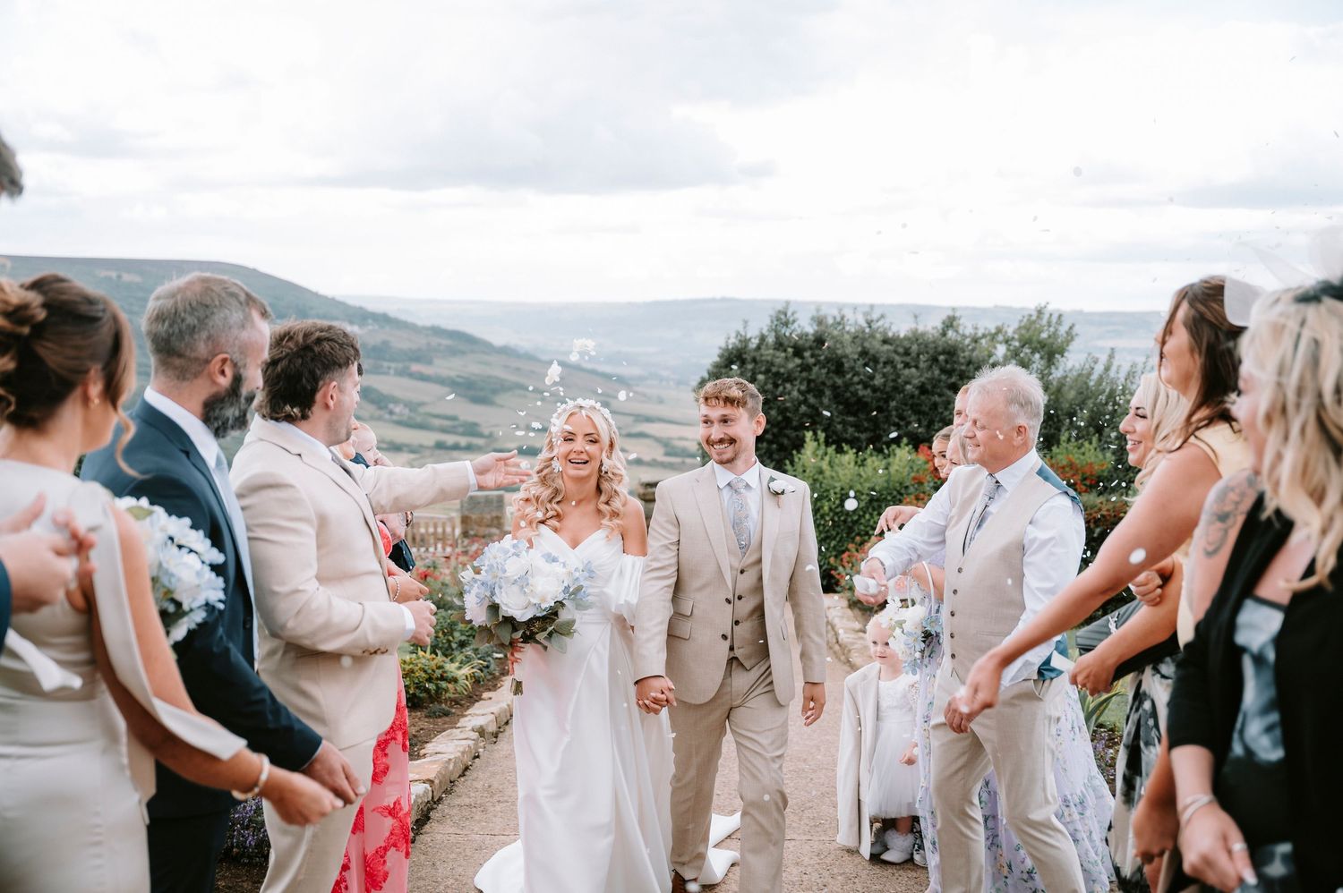 Wedding party celebrates with joyful dancing and embraces during an outdoor reception in natural lighting.