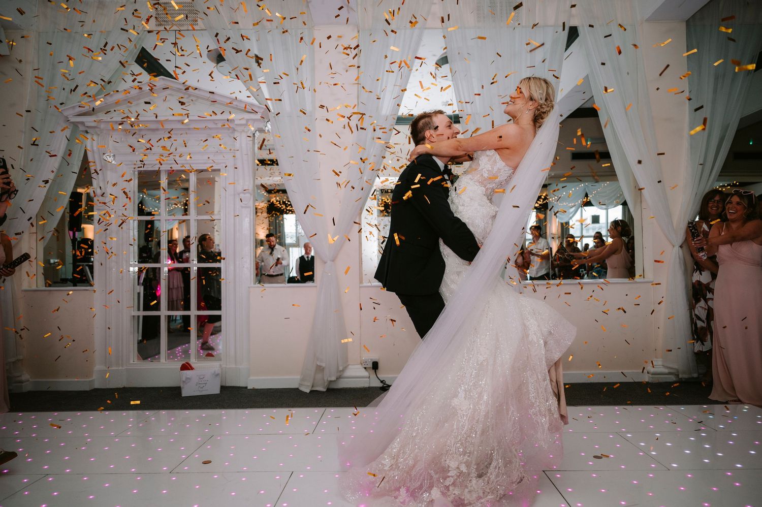 Bride and groom share their first dance as confetti falls around them in a beautifully decorated venue.