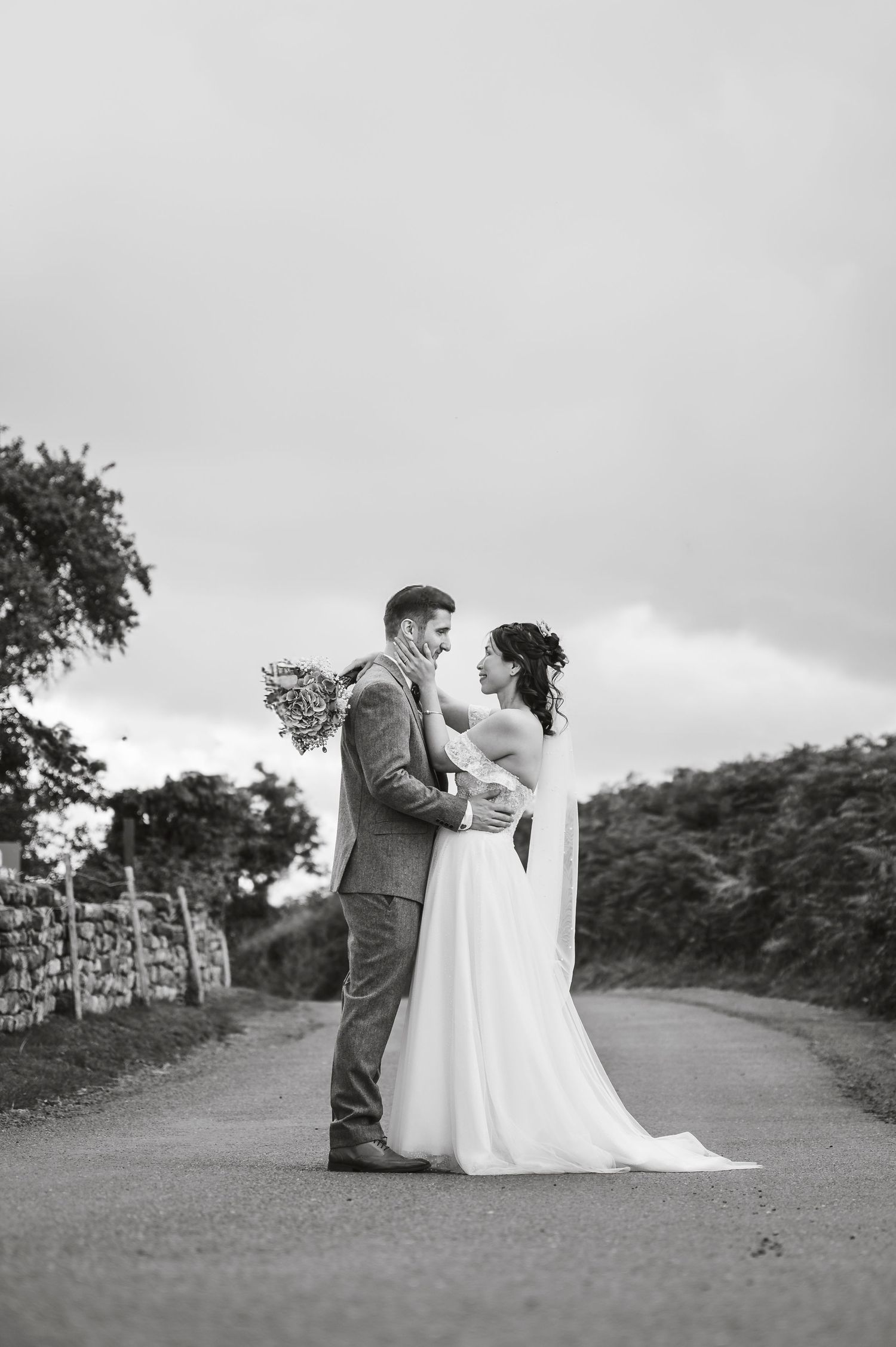 Black and white romantic wedding photos of a couple sitting together on a countryside path with stone walls.