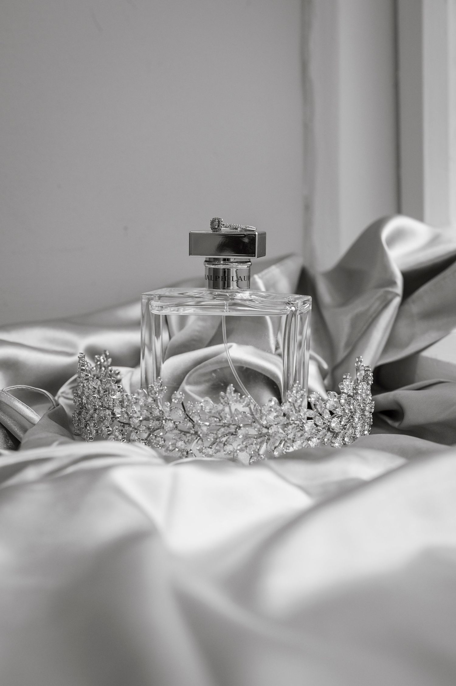 Wedding accessories including perfume bottle and crystal tiara displayed on white silk fabric.