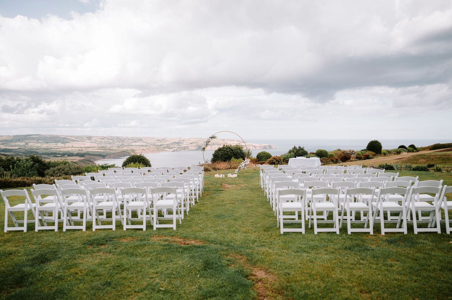 Outdoor wedding ceremony setup with white chairs arranged on a scenic hilltop overlooking the landscape.