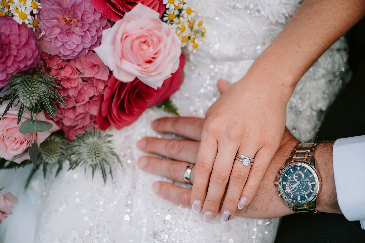 Close-up of wedding rings and floral details on a white dress.
