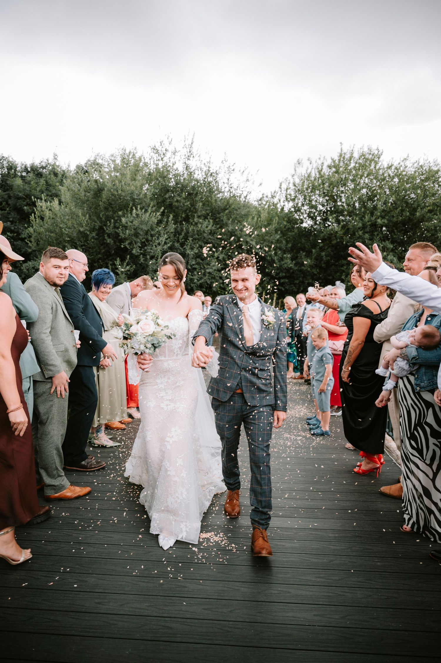 Wedding party and guests celebrate with confetti on an outdoor deck.