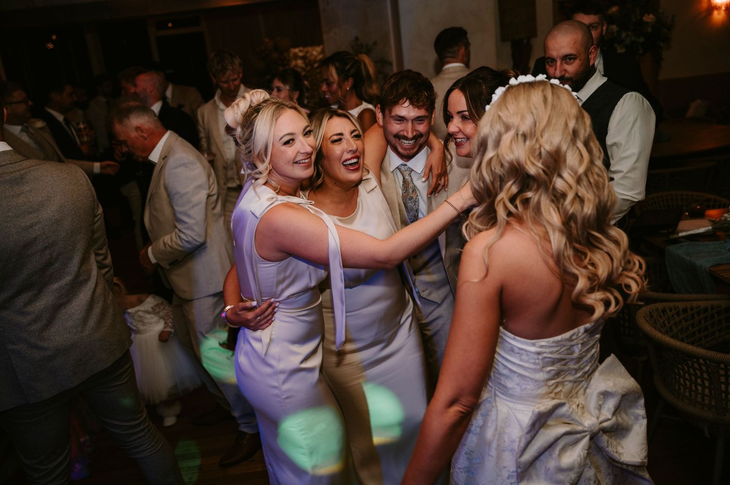 Wedding reception guests dancing and celebrating on a lively dance floor with colorful lighting.