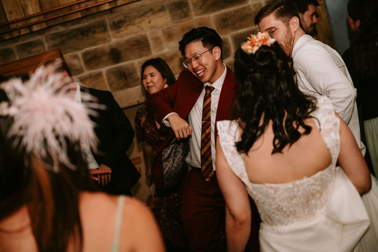 Dancing and celebration at a wedding reception in a dimly lit venue with stone walls.