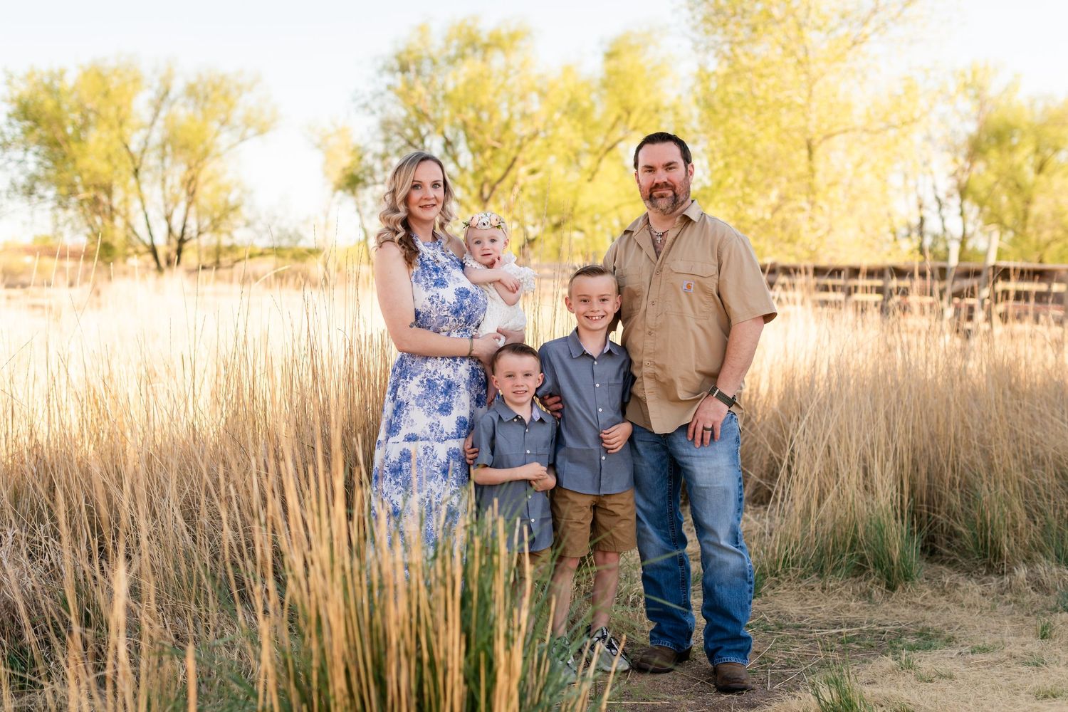 Family of five posing outdoors in golden field with tall grass and trees during sunset photo session. Mini sessions photography Longmont Co