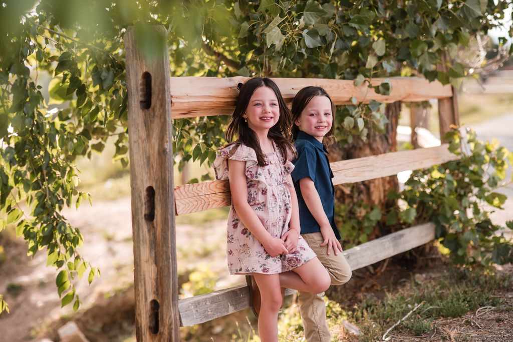 Siblings on wooden gate with cottonwood leaves during a seasonal fall portrait shoot at Golden Ponds in Longmont CO.