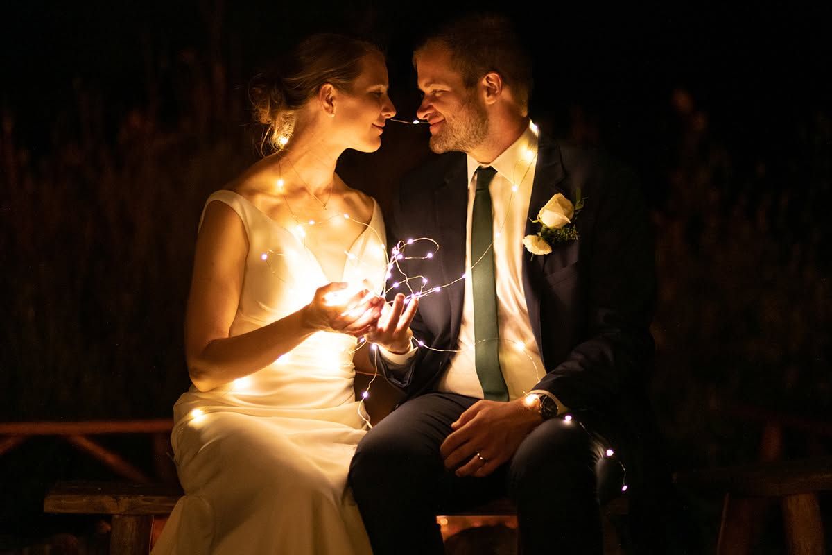 Bride and groom sitting together at night holding sparklers, sharing a romantic moment in wedding attire. Blue Hour wedding photography