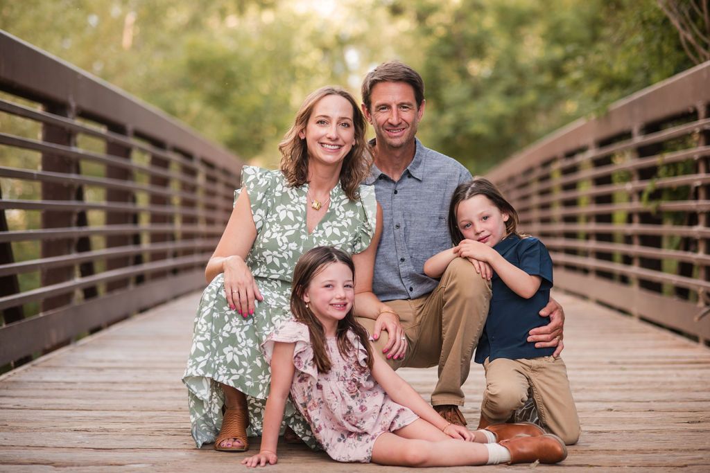 A family of four pose on the bridge during a autumn mini session at Golden Ponds Nature Area in Longmont Colorado