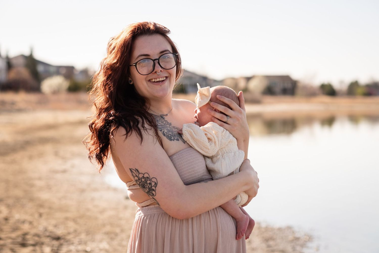 Photo of a warm family moment, featuring a mother holding her baby while sitting by the serene lakeside at McIntosh Lake in Longmont, Co.