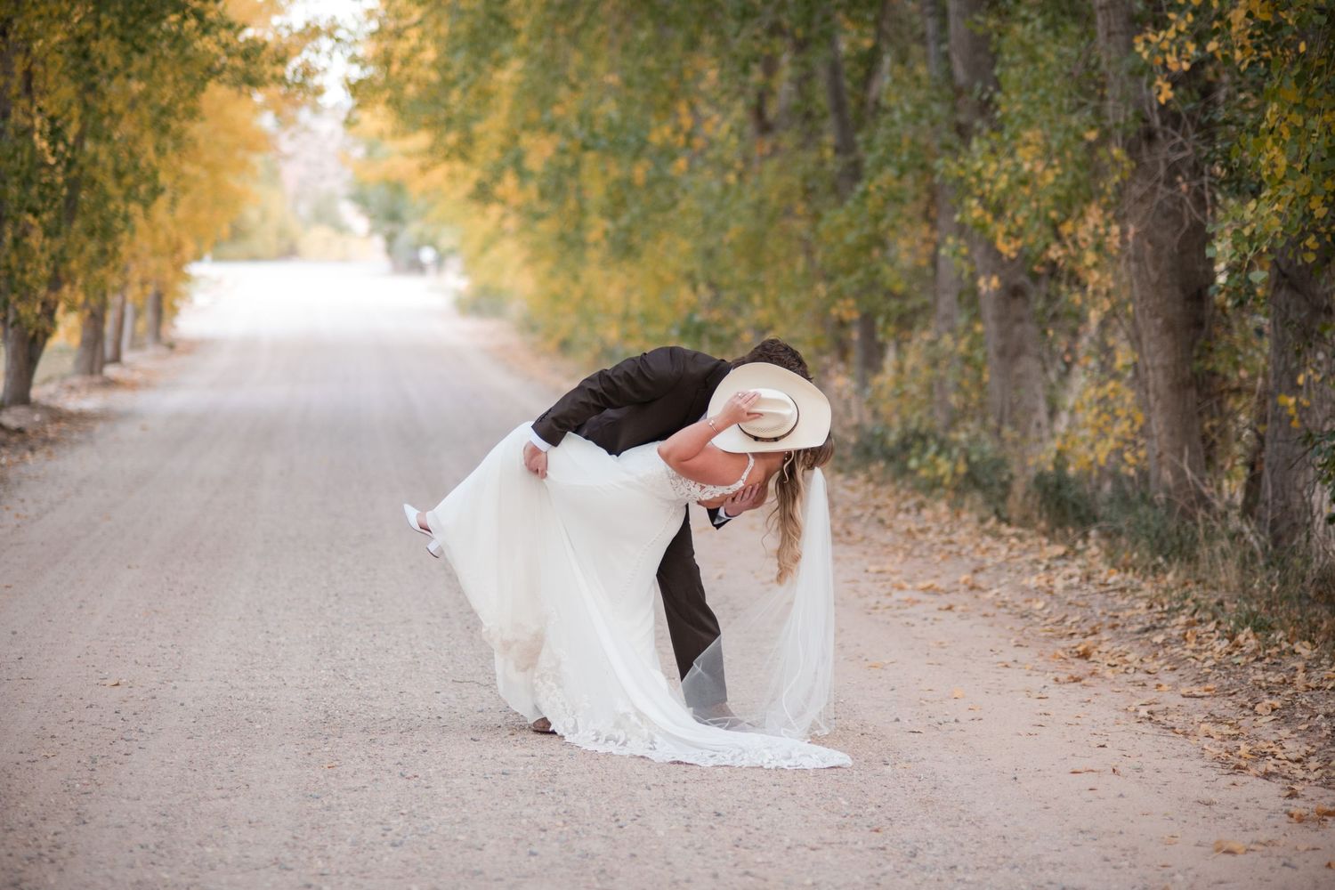 Fall wedding road photo: couple poses for a kiss with a country vibe, a hat covering the kiss. Ellis Ranch Venue Angelice Caballer photo