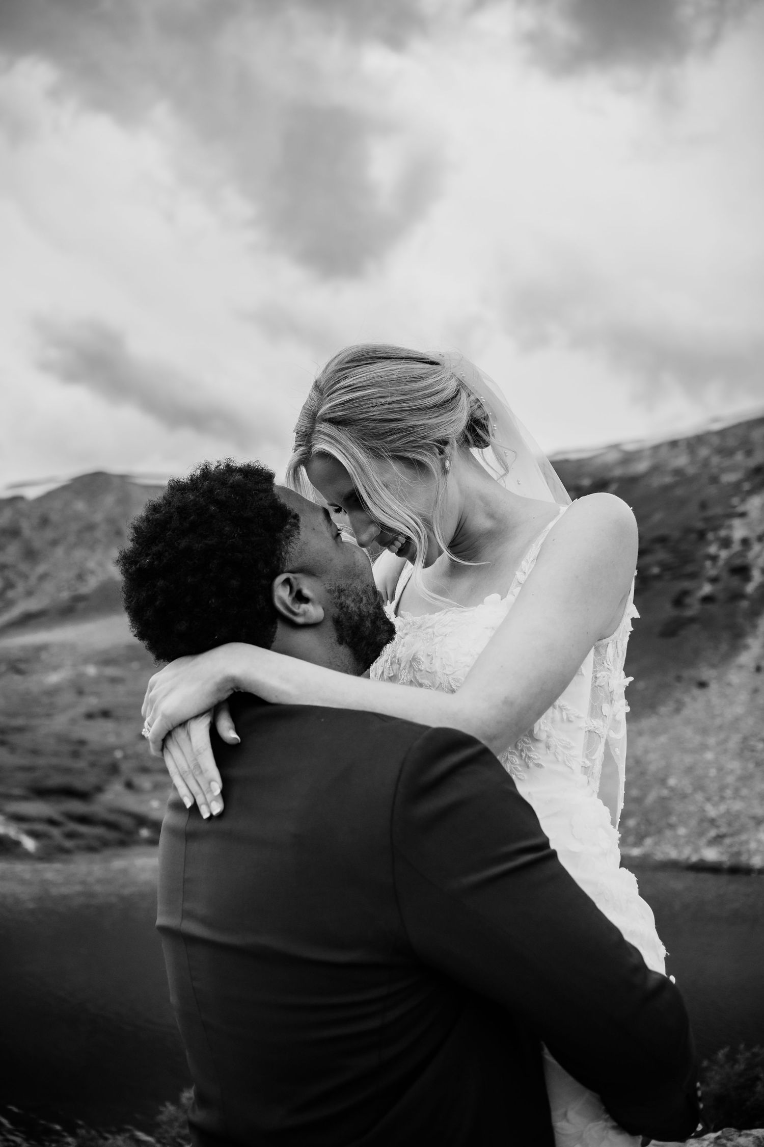 Black and white photo of a bride and groom sharing a romantic moment outdoors with mountains in the background. Loveland Ski Resort