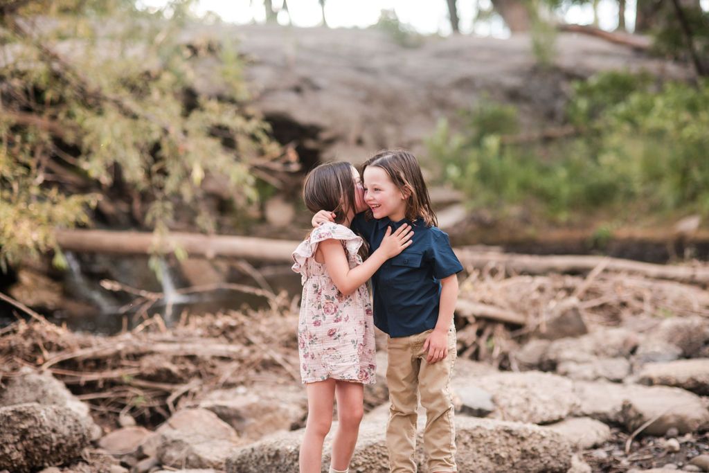 Siblings laughing while playing near the waterfall during a seasonal fall portrait shoot at Golden Ponds in Longmont CO.