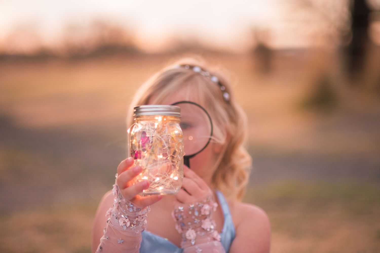 Young girl holding a glowing mason jar with fairy lights outdoors at golden hour sunset. Creative photo session, Sandstone Ranch Co