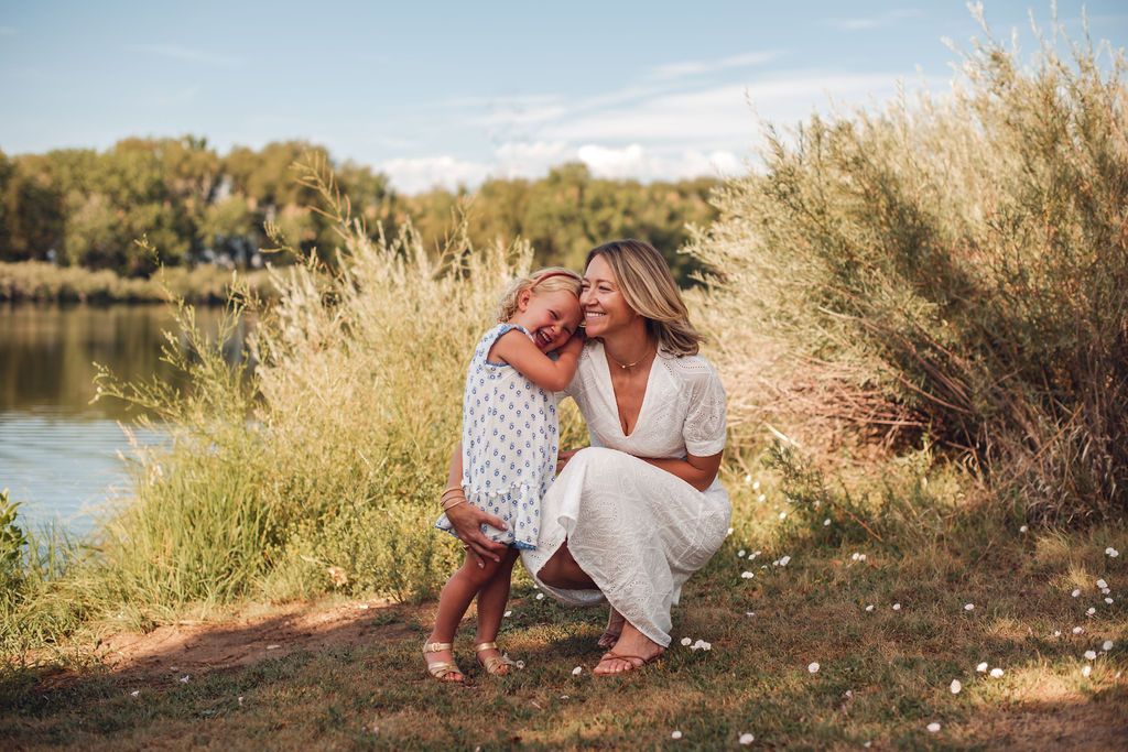 A candid, joyful close-up portrait of a mother and daughter laughing near the waterfront at Golden Ponds Park in Longmont.