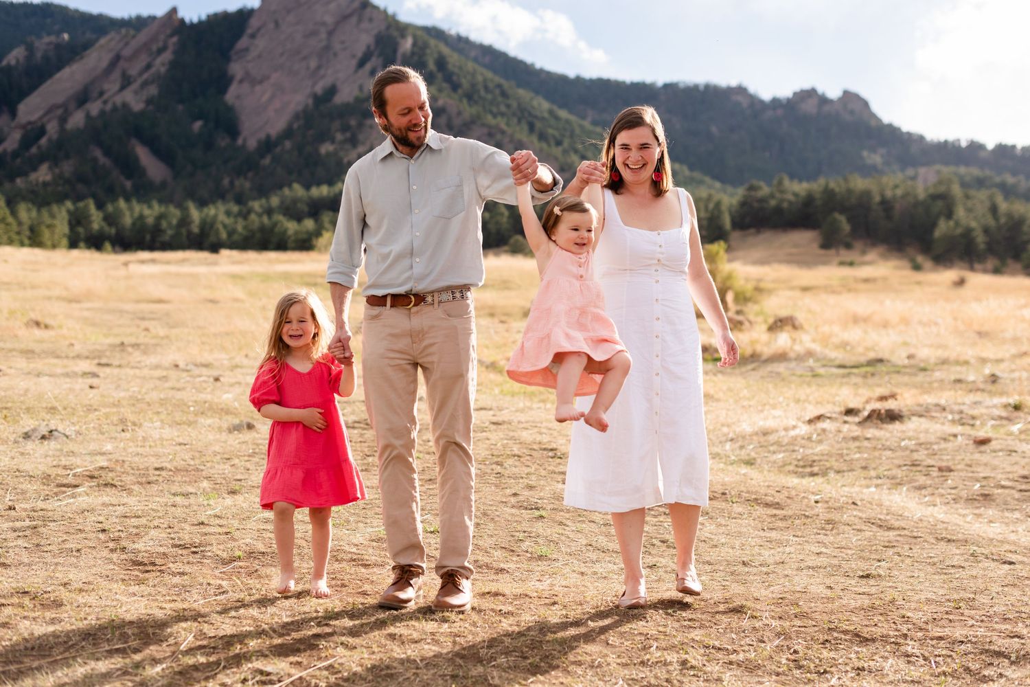 Family sunset photography: having fun with Mom and Dad swinging their baby girl at Chautauqua Park, Boulder, CO, with the Flatirons.