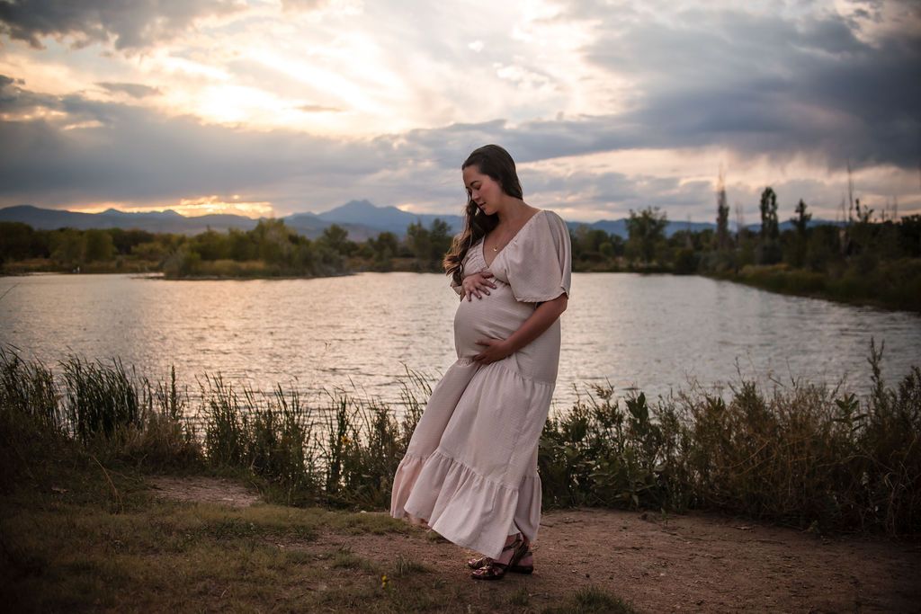 A stunning golden hour maternity portrait silhouette overlooking the lake and Front Range mountains at Golden Ponds Nature Area.