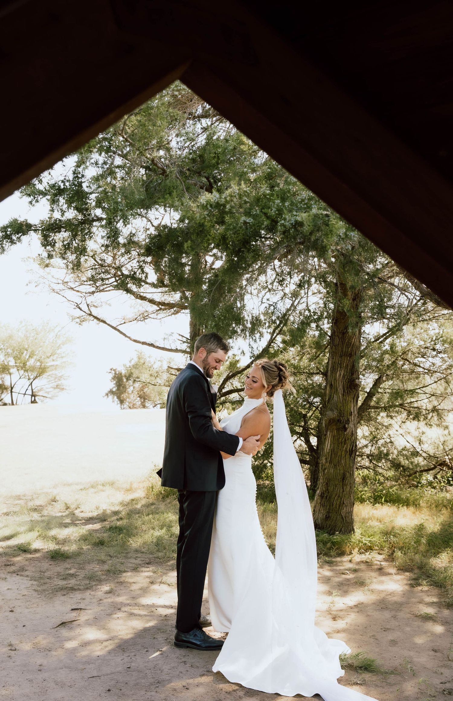 A romantic first look moment between a couple in formal wedding attire under tall trees on a sunny day.
