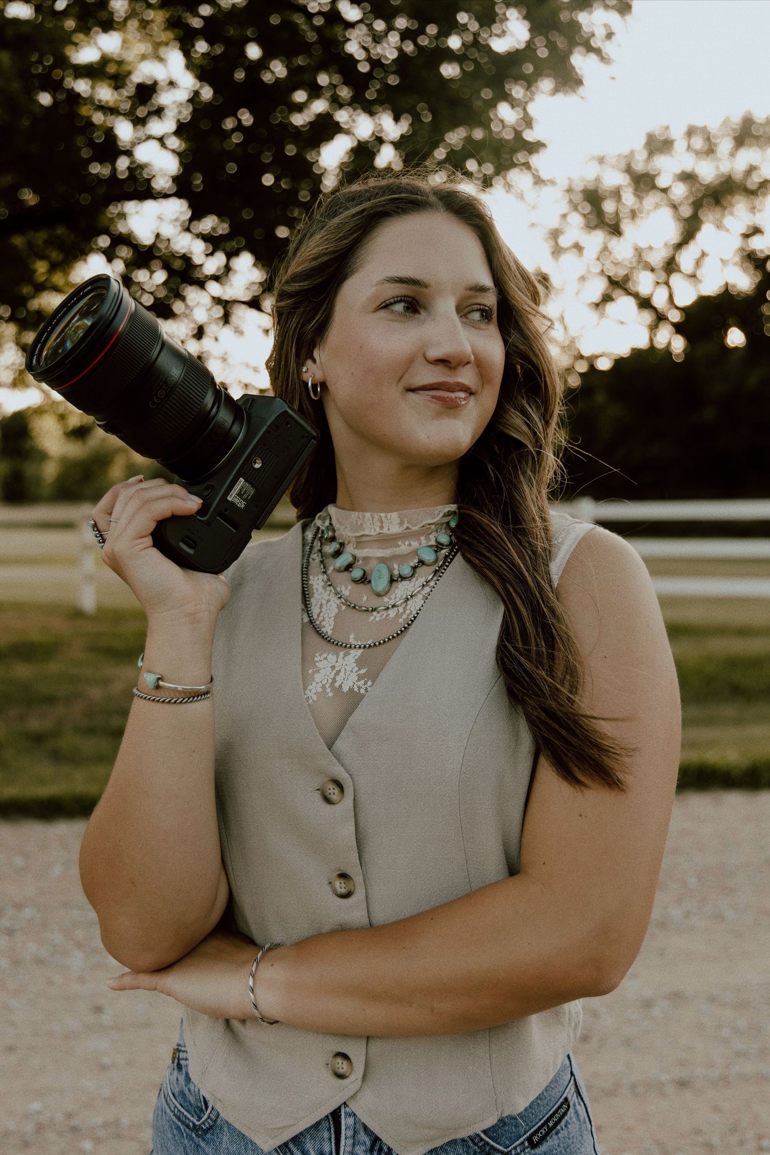 A woman in a tan vest poses outdoors during golden hour with natural lighting and dramatic shadows.