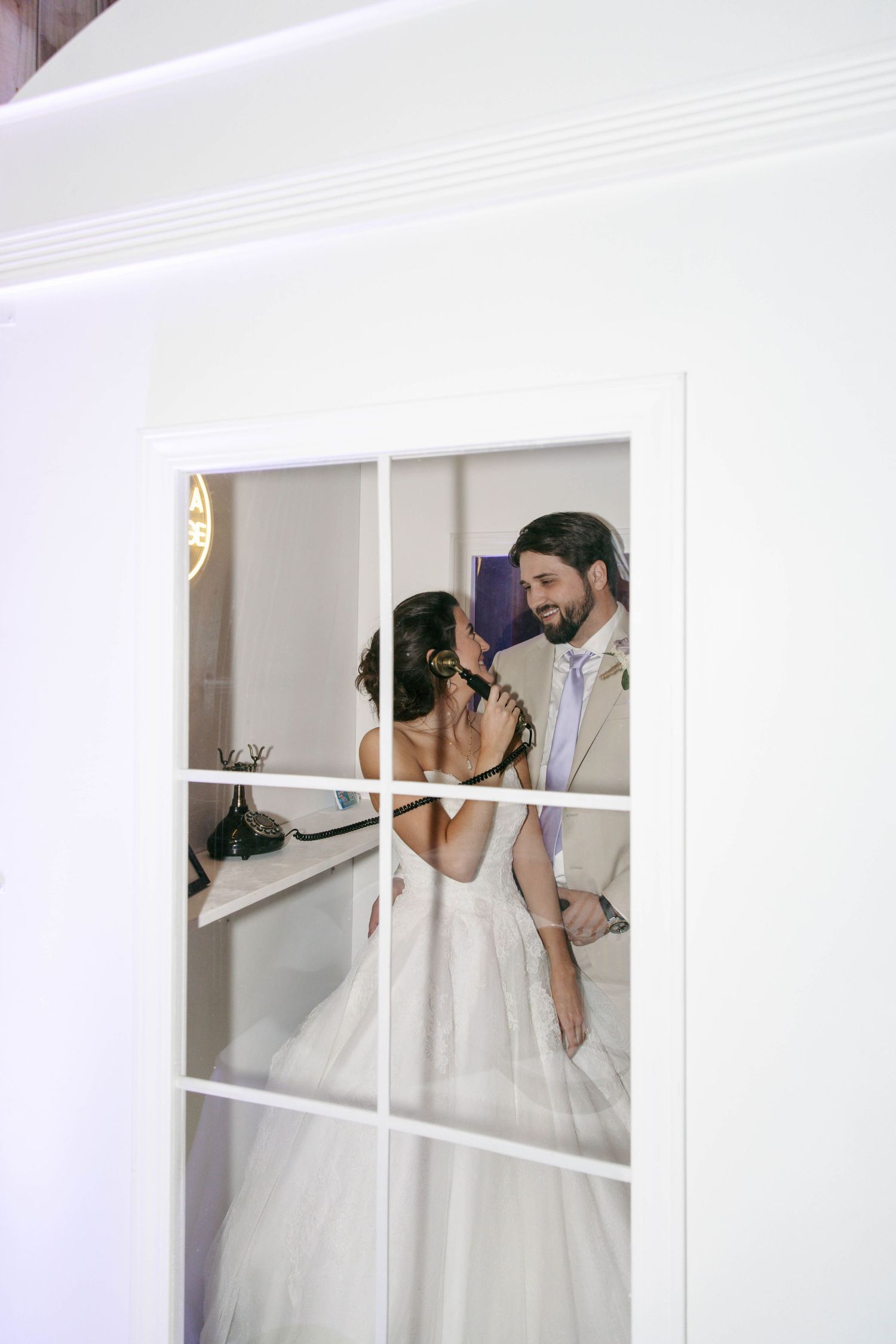 Bride and groom share a romantic moment through glass French doors at their elegant wedding reception.