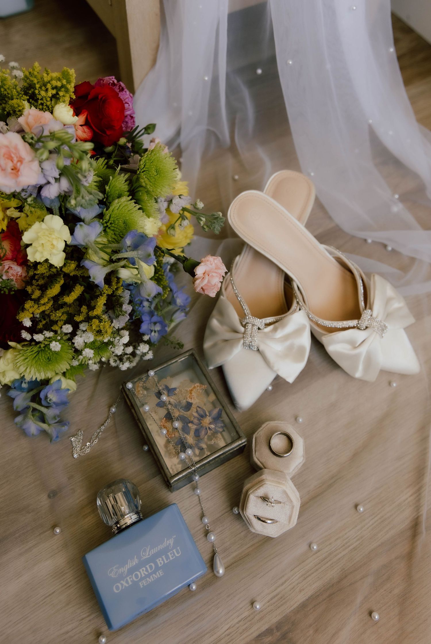 Wedding accessories including elegant cream bridal shoes, floral bouquets, and delicate decor arranged on wooden surface.