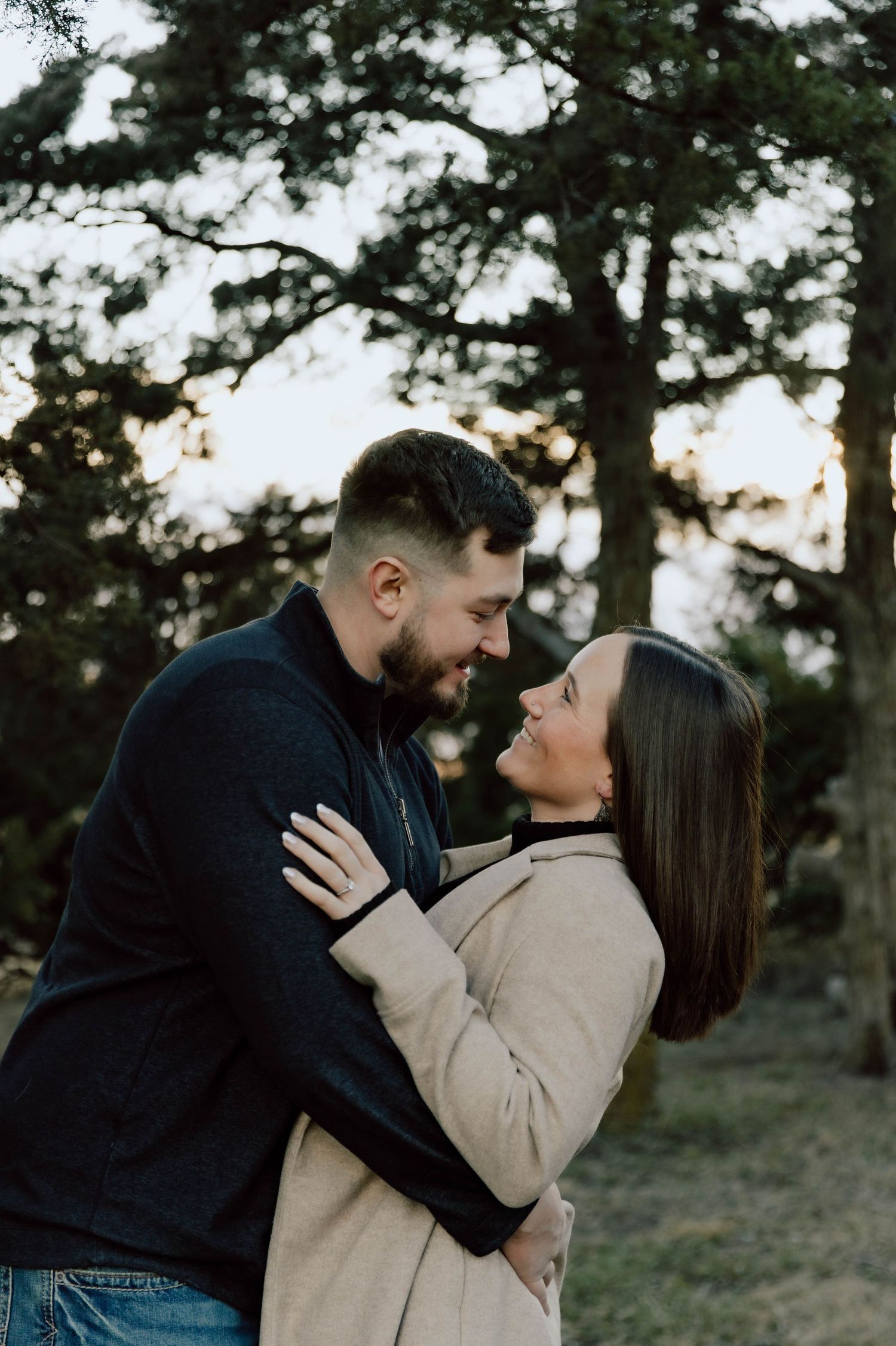 A romantic couple embraces and shares tender moments in a wooded outdoor setting during golden hour.