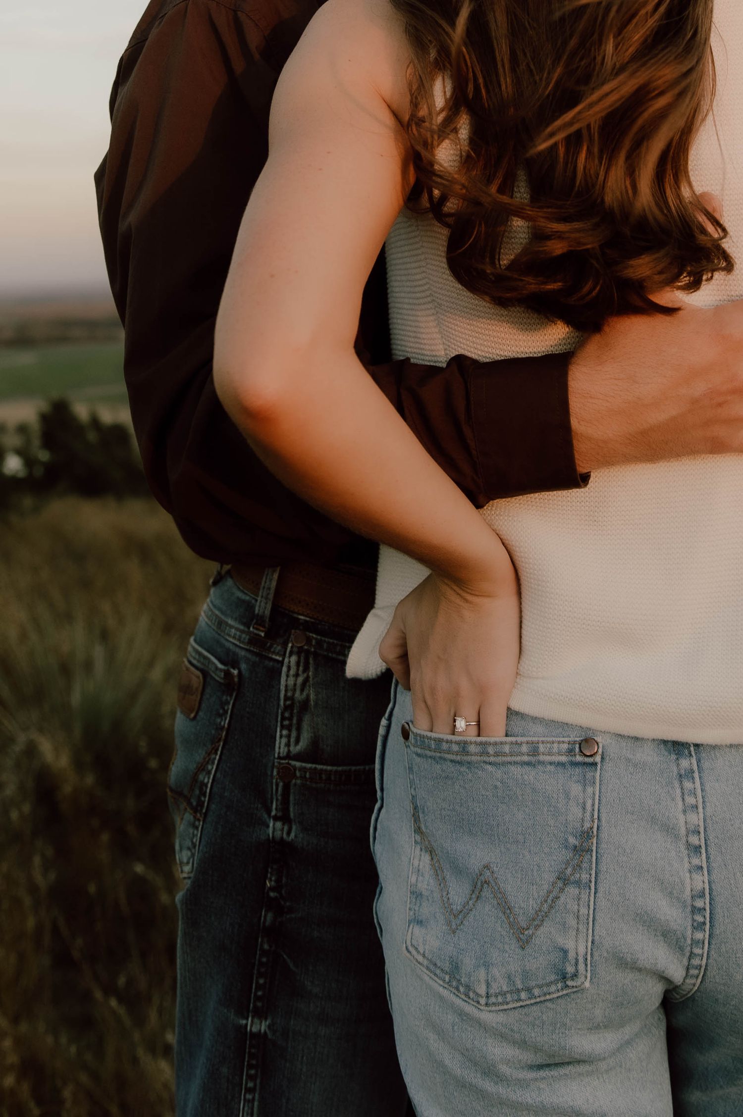 Close-up series of a couple embracing while wearing jeans and casual clothing at sunset in a field.