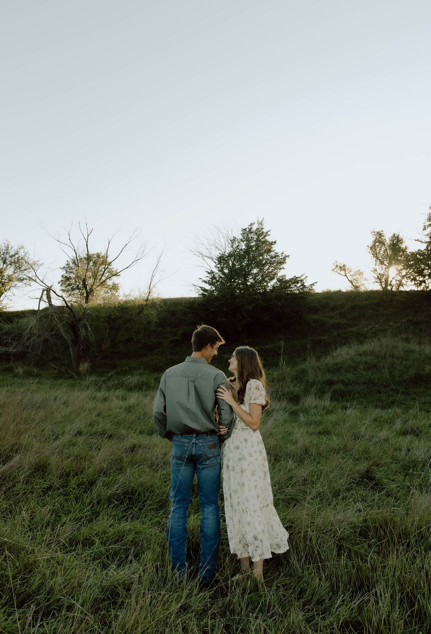 A couple walking together through a grassy hillside at sunset, holding hands and enjoying the peaceful moment.
