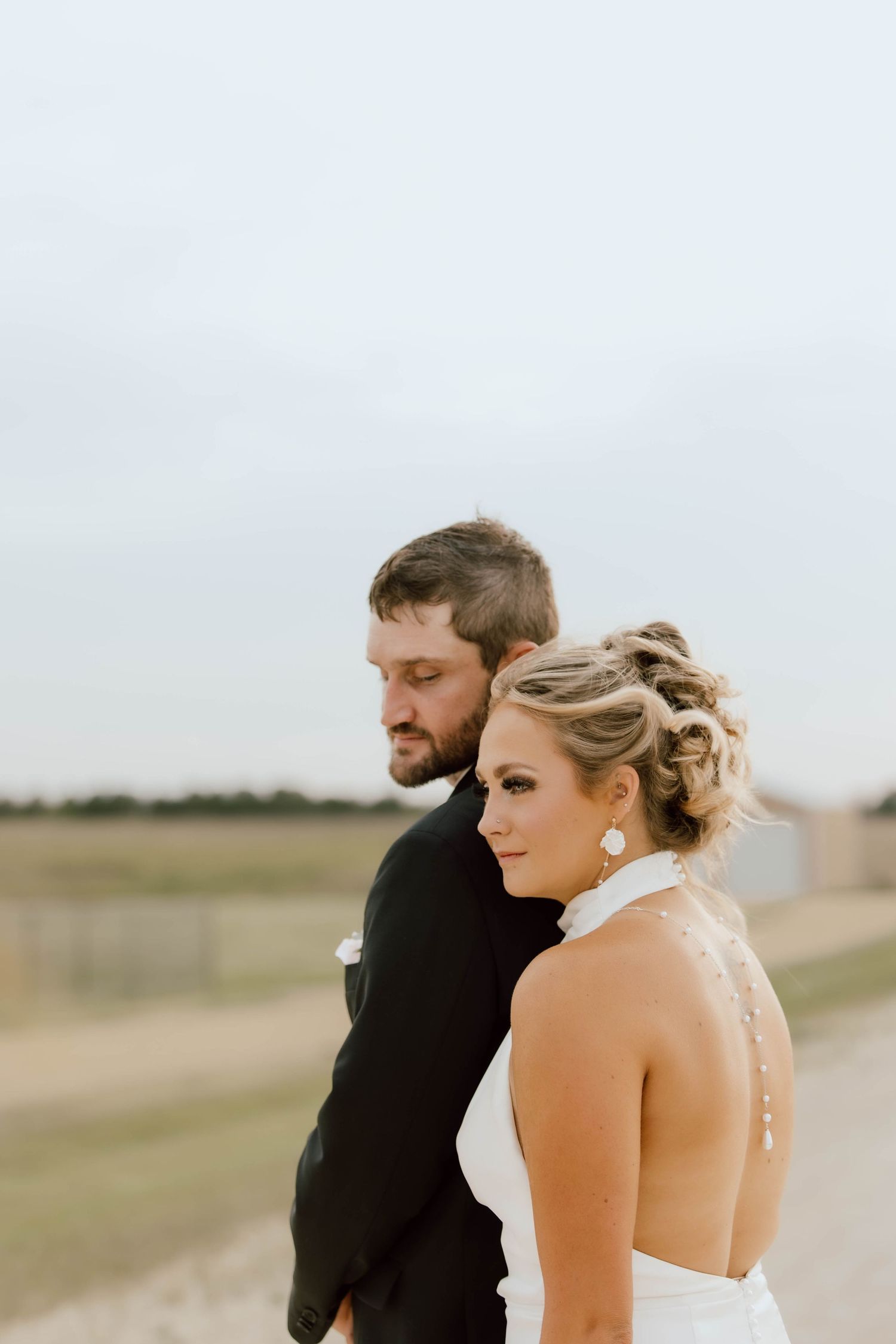 A couple in wedding attire standing together in a field during golden hour, with soft natural lighting.